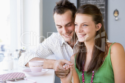 Ein junges Pärchen sitzt Händchen haltend im Cafè