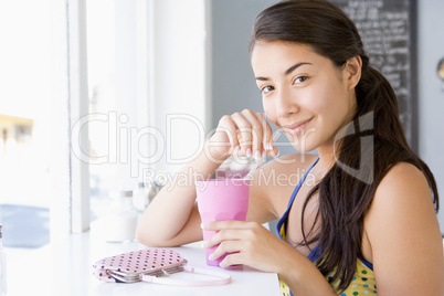 Eine junge dunkelhaarige Frau sitzt im Cafè und nimmt ein Getränk zu sich