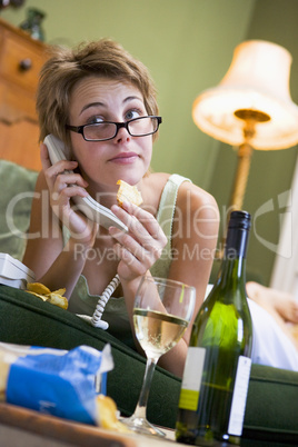 A young woman in her pyjamas on the phone and drinking wine