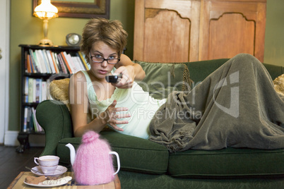 A young woman lying on her couch watching television