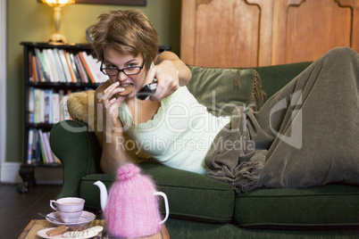 A young woman lying on her couch watching television