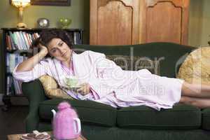 A young woman lying on her couch drinking tea