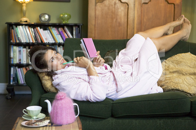 A young woman lying on her couch writing in her journal