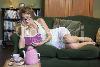 A young woman lying on her couch writing in her journal