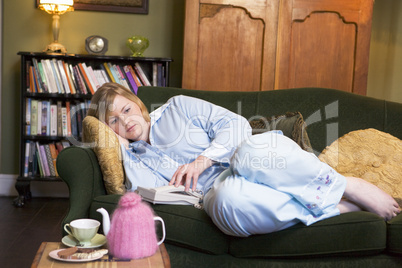 A young woman lying on her couch reaching for the phone