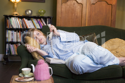 A young woman lying on her couch talking on the phone