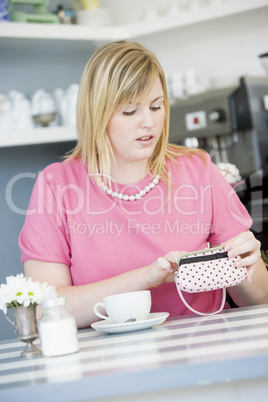 A young woman sitting in a cafe looking worried into her purse