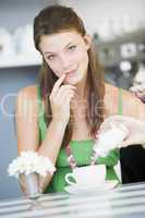 A young woman sitting in a cafe pouring sugar into her tea