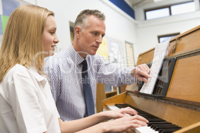 Teacher with schoolgirl playing piano in music class