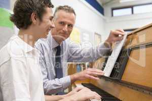 Teacher with schoolboy playing piano in music class