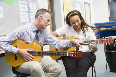 Schoolgirl and teacher playing guitar in music class
