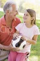 Grandfather and granddaughter outdoors with ball smiling