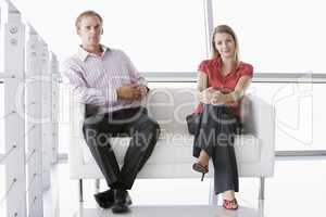 Two businesspeople sitting in office lobby smiling