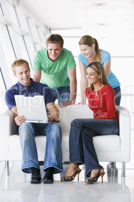 Four people in lobby looking at laptop smiling