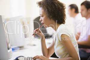 Woman in computer room looking at monitor and thinking