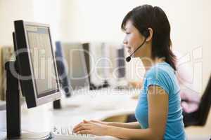Woman wearing headset in computer room typing and smiling