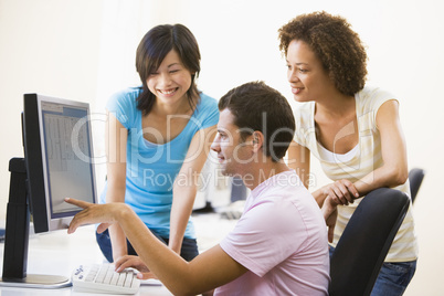 Three people in computer room pointing at monitor and smiling