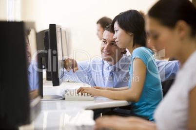 Man assisting woman in computer room smiling
