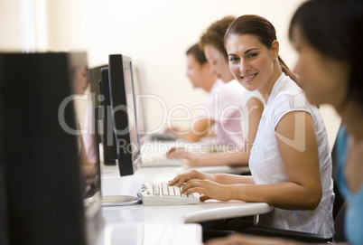 Four people sitting in computer room typing and smiling