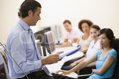 Man with clipboard giving lecture in computer class