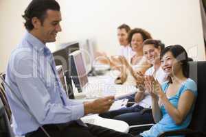 Man with clipboard giving lecture in applauding computer class