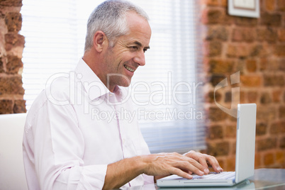 Businessman sitting in office typing on laptop smiling