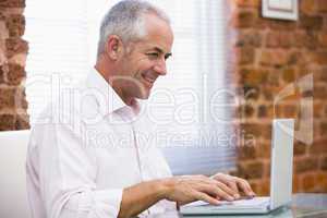 Businessman sitting in office typing on laptop smiling