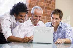 Three businessmen sitting in office with laptop smiling