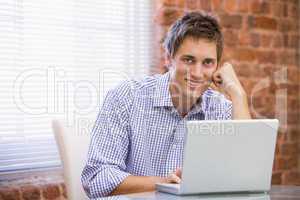 Businessman sitting in office with laptop smiling