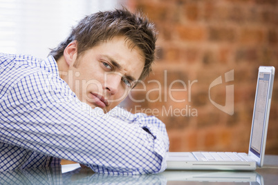 Businessman sitting in office with laptop looking unhappy