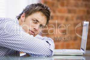 Businessman sitting in office with laptop looking unhappy