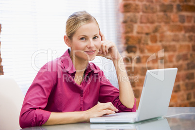 Businesswoman sitting in office with laptop smiling