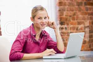 Businesswoman sitting in office with laptop smiling