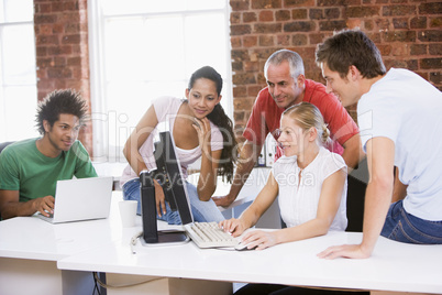 Five businesspeople in office space looking at computer and smil