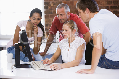 Four businesspeople in office space looking at computer smiling