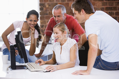 Five businesspeople in office space looking at computer smiling