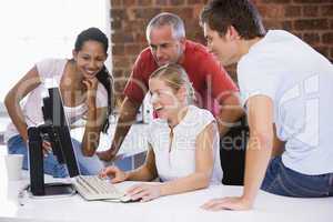 Five businesspeople in office space looking at computer smiling