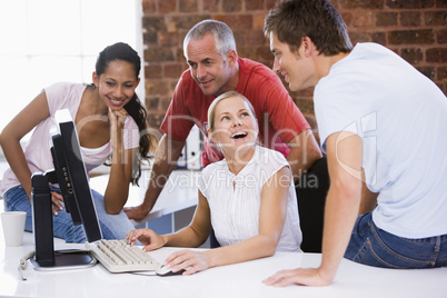 Four businesspeople in office space with computer smiling