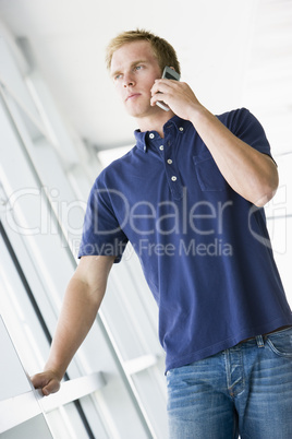 Man standing in corridor smiling using cellular phone