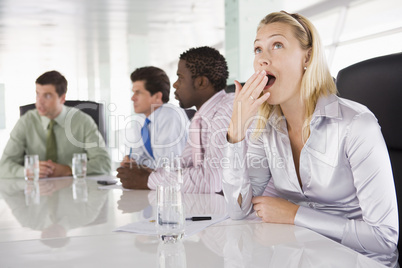 Four businesspeople in boardroom with one businesswoman yawning