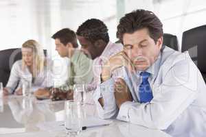 Four businesspeople in boardroom with one businessman sleeping