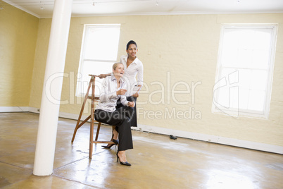 Two women in empty space with ladder holding paper and smiling