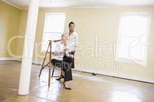 Two women in empty space with ladder holding paper and smiling