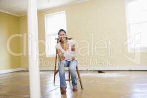Woman sitting on ladder in empty space holding paper smiling