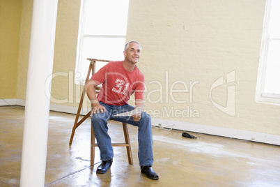 Man sitting on ladder in empty space holding paper