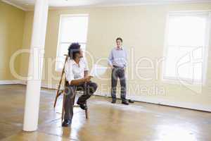 Man sitting on ladder in empty space holding paper talking to ot