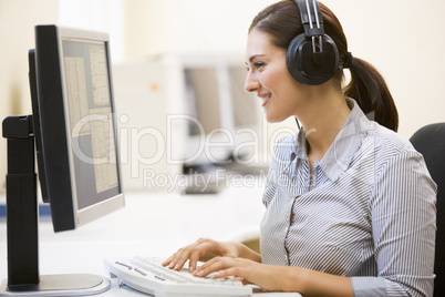 Woman wearing headphones in computer room typing and smiling