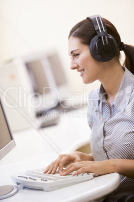 Woman wearing headphones in computer room typing and smiling