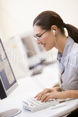 Woman in computer room listening to MP3 Player while typing and