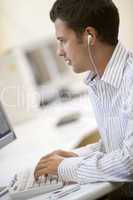Man in computer room listening to MP3 player while typing